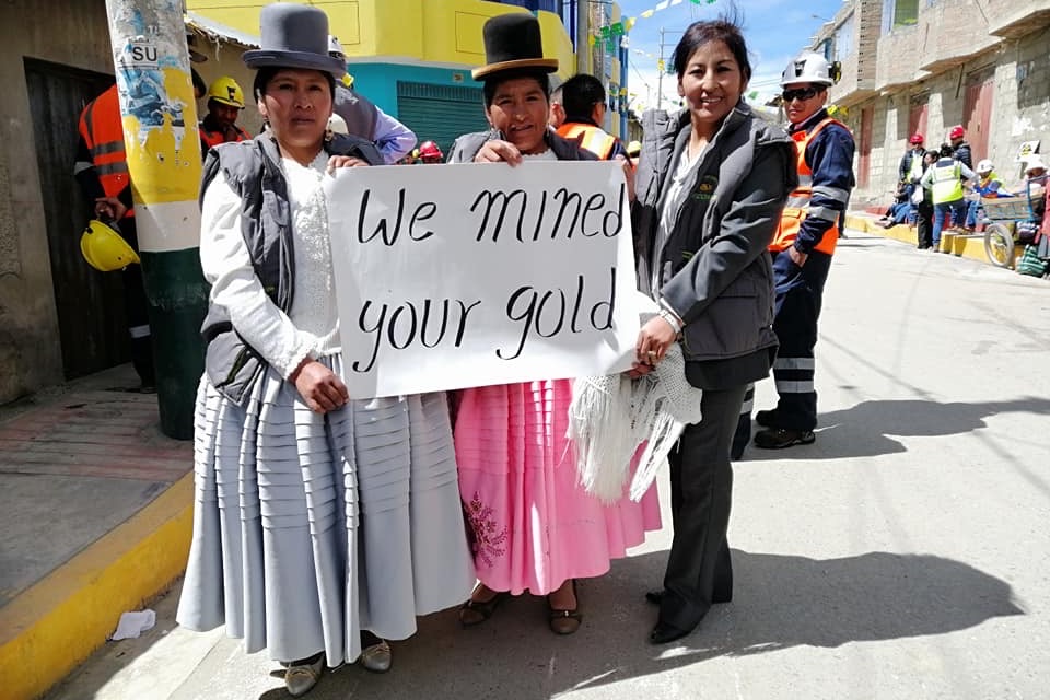 Three women from a Fairmined certified mining organisation in Peru holding a sign reading We mined your gold